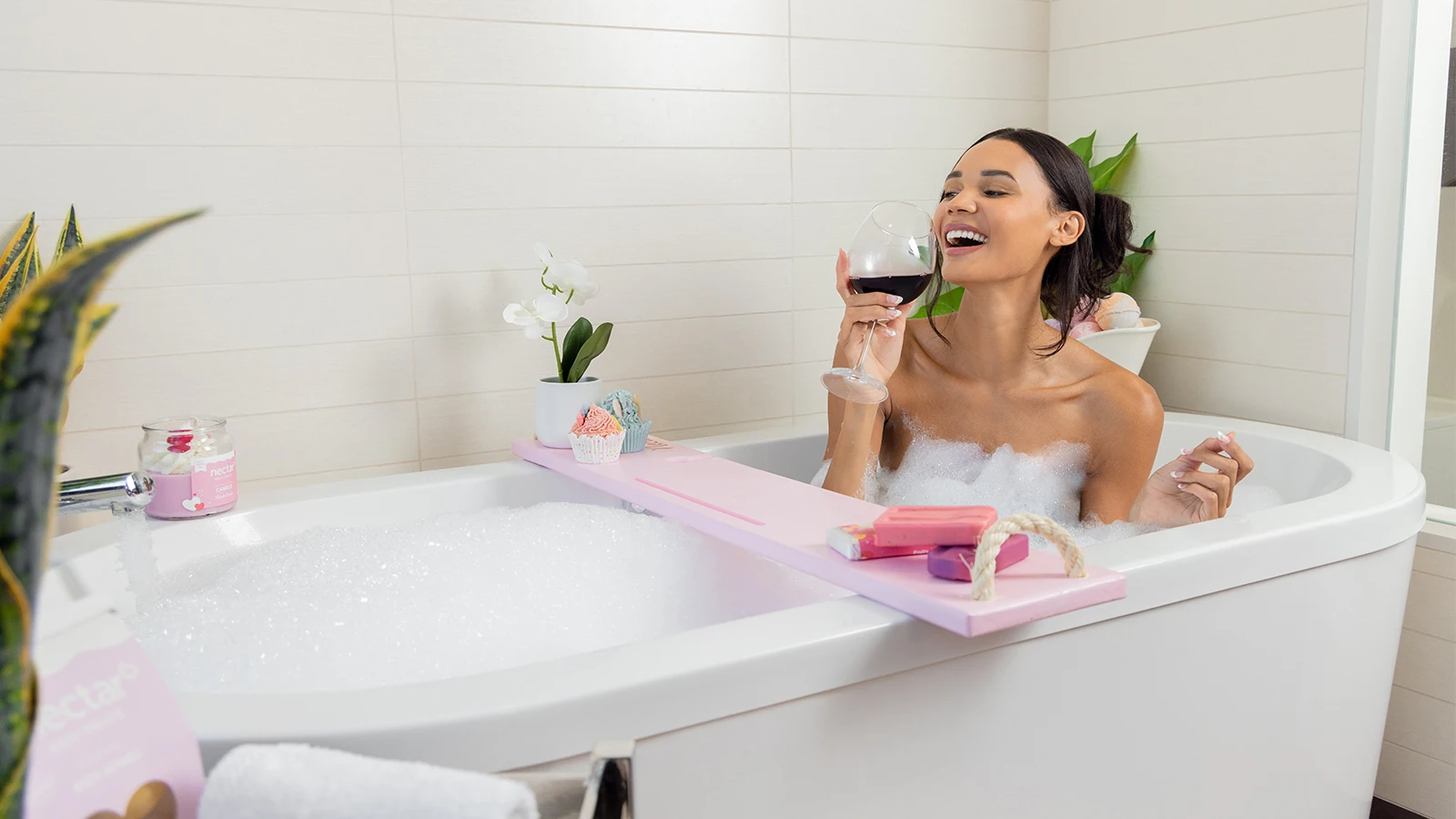 A woman in a pink bath tub drinking wine.