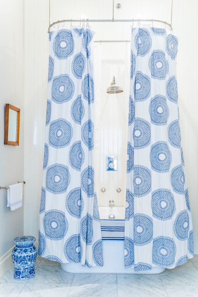 Blue and white shower curtain with an oval motif surrounds bathtub.