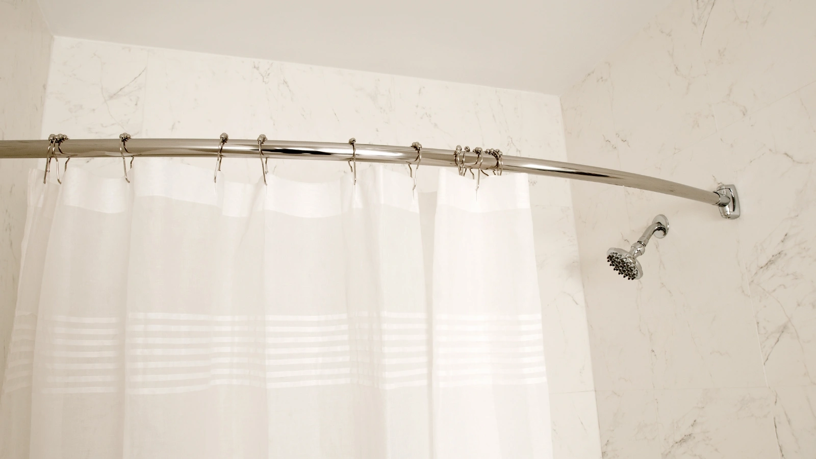 Can You Use a Shower Curtain Without a Liner? A bathroom with a white shower curtain and a chrome shower rod.