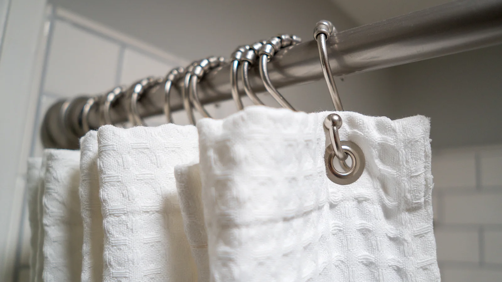 A white towel hangs on a metal rod in a bathroom, alongside a closed shower curtain which show how to keep shower curtain closed.