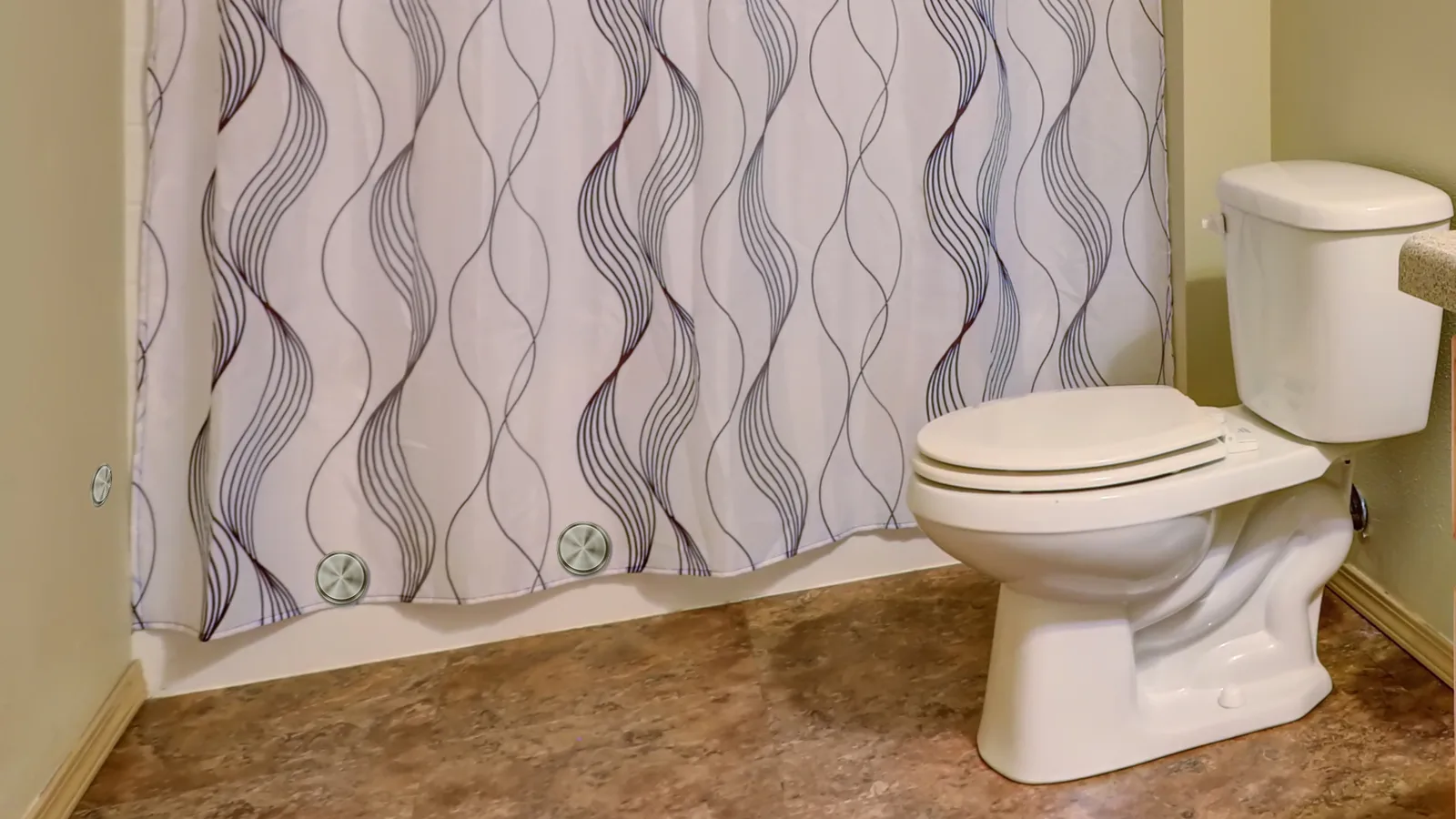 A bathroom with a toilet and shower curtain that stays closed shows how to keep shower curtain closed.