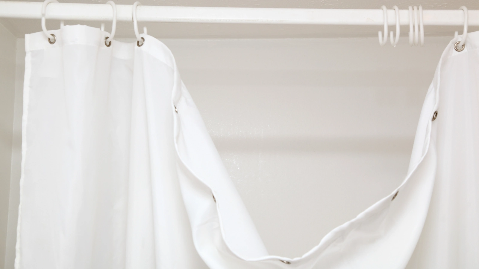 Should You Leave Shower Curtain Open or Closed? A white shower curtain hanging on a hook.