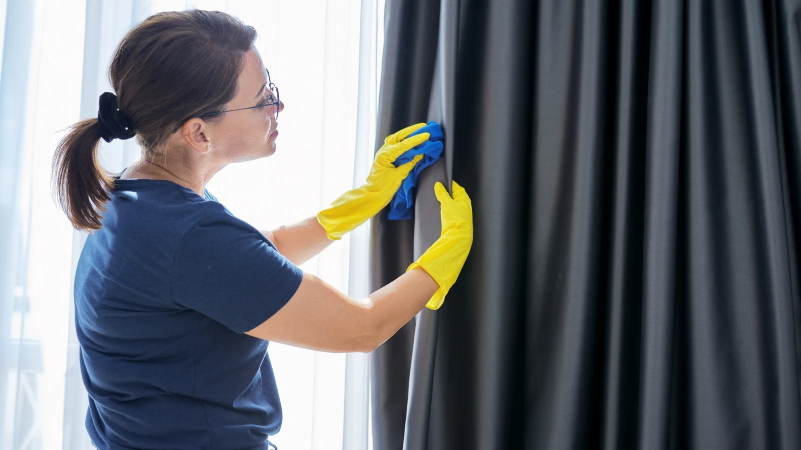 Should You Leave Shower Curtain Open or Closed? A woman in yellow gloves cleaning a black curtain.