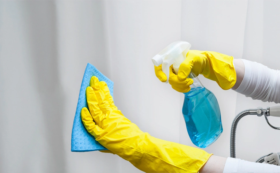 A woman wearing yellow gloves is cleaning a bathroom with a shower curtain smells like urine.